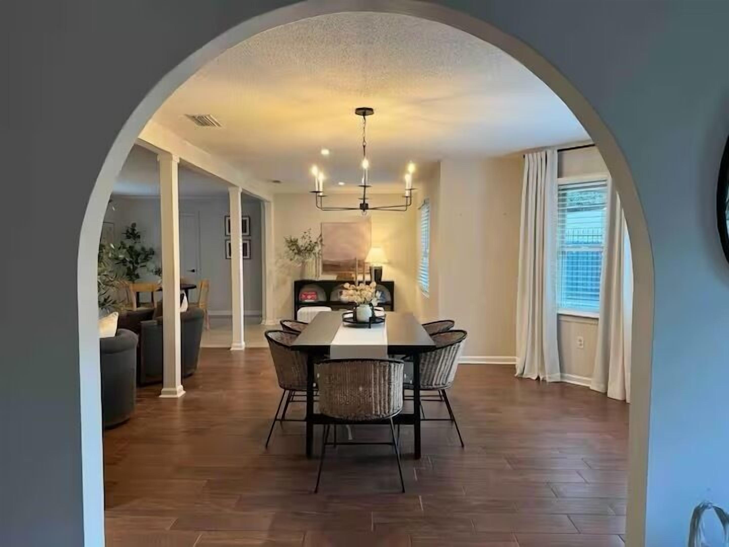 Un comedor con una mesa y sillas, un arco de entrada y vistas a una sala de estar con un sofá y una planta.