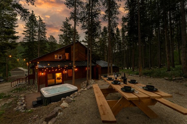 A cabin with a hot tub, dining table, and outdoor lights.