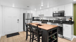 A modern kitchen with white cabinets, stainless steel appliances, and a wooden dining table. - Cozy Creekside Condo with Resort-Style Amenities (Branson)