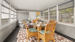 Una sala de estar con ventanales, una mesa de comedor, sillas de mimbre y vistas al exterior.
