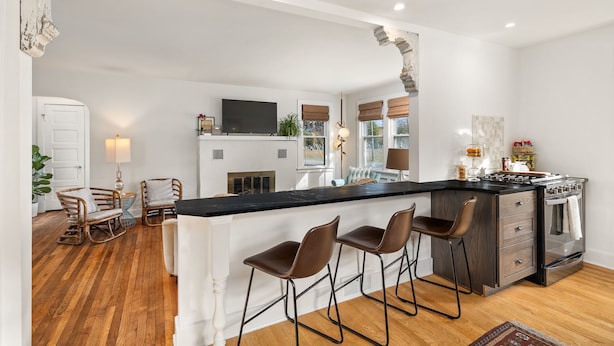 Una cocina moderna con una isla central, taburetes de bar, horno empotrado y un amplio ventanal con persianas.