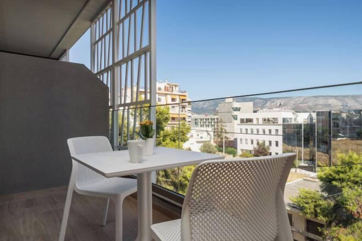 A balcony with a table and chairs, offering a view of buildings and greenery.