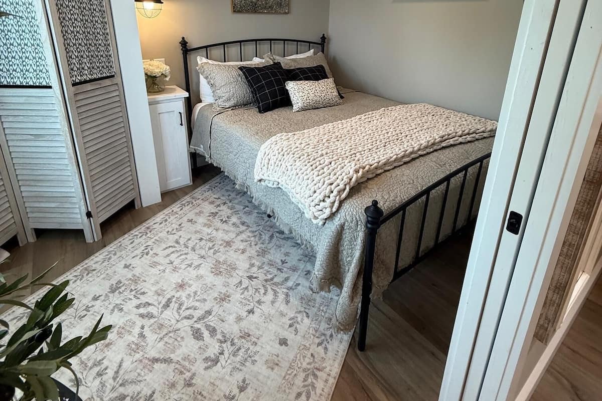 A bedroom with a bed, bedside tables, a lamp, an air conditioning unit, and a patterned rug.