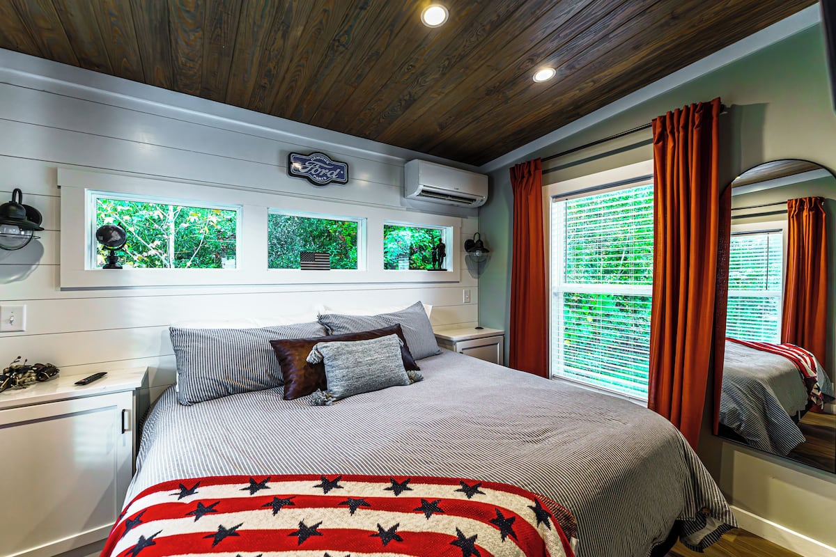 A bedroom with a bed, a window with blinds, a ceiling fan, and a wall-mounted air conditioner.