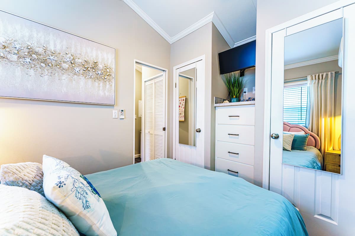 A bedroom with a bed, a dresser, a mirror, and a painting on the wall.