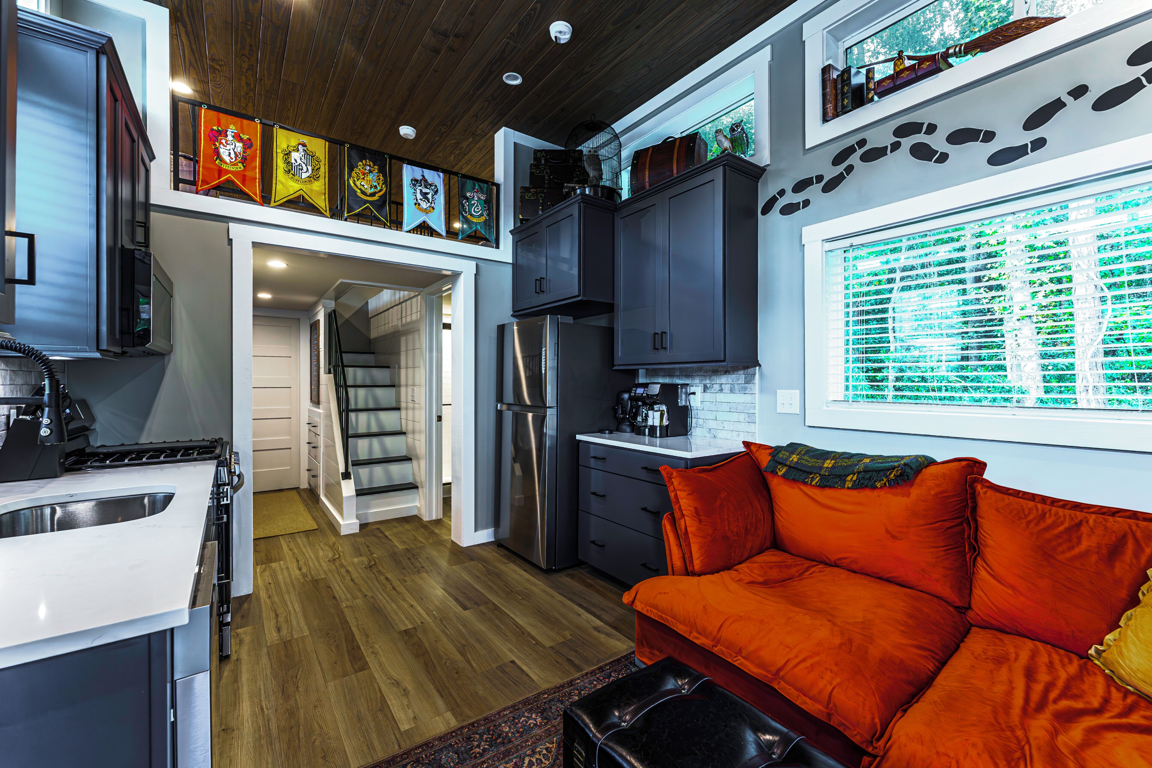 A compact kitchen with modern appliances, a dining area with a red sofa, and a staircase leading to an upper level.