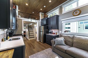 A modern kitchen with a central island, a dining area with a sofa, and a staircase leading to an upper level. - Island Oaks RV Resort (Glen St. Mary)