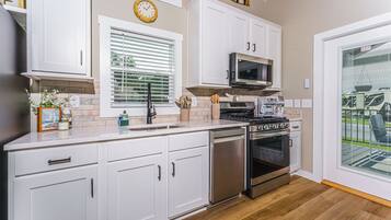 A modern kitchen with white cabinets, stainless steel appliances, a clock, and a view of the outdoors through a glass door.