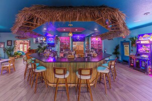Una zona de bar con techo de paja, taburetes de madera y un letrero de neón.