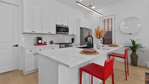 A modern kitchen with white cabinetry, a central island, red chairs, and a large mirror on the wall. - Elevated Luxury 3BR • Mins to NRG • Med Center • Downtown • GRB (Houston)