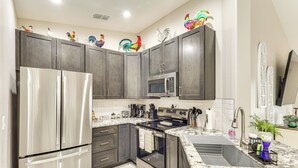 Uma cozinha moderna com armários escuros, eletrodomésticos de aço inoxidável e figuras decorativas de galos na parede.