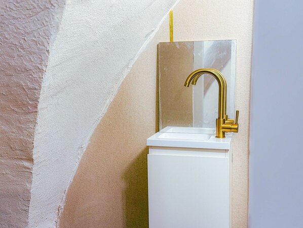 A bathroom with a white sink, gold faucet, and a mirror. - roga bjeruslem (Jerusalem)
