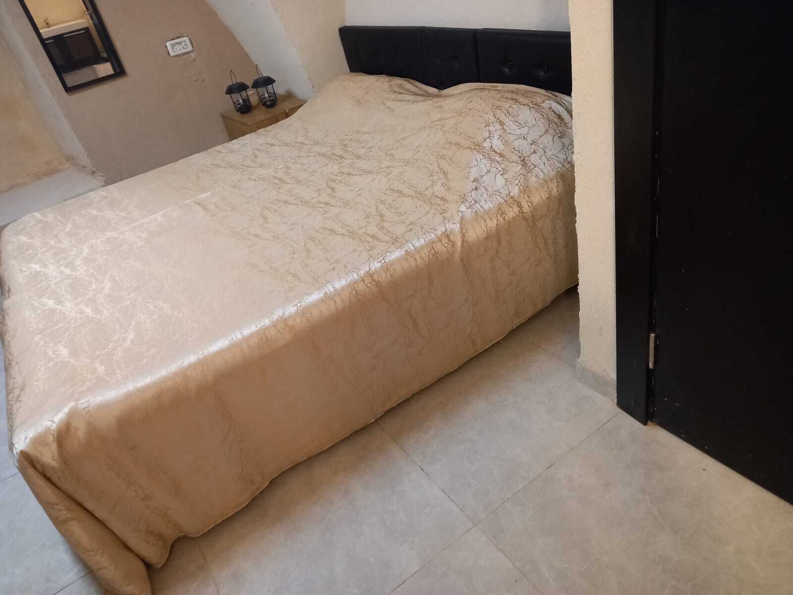 A bed with a beige cover, a black headboard, and a tiled floor.