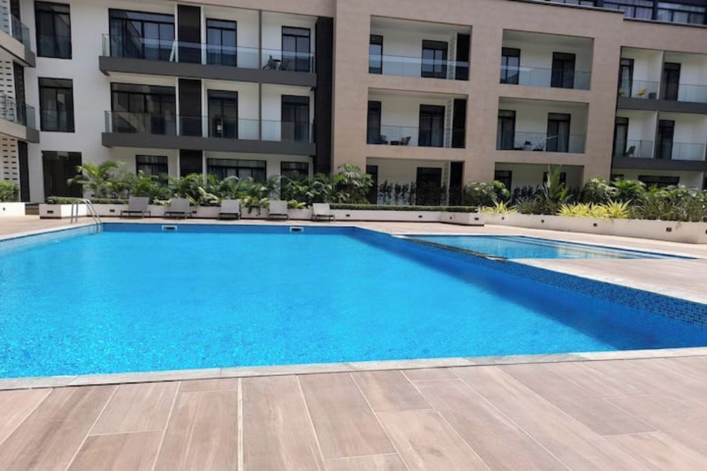 A modern building with a rectangular swimming pool surrounded by a tiled deck.