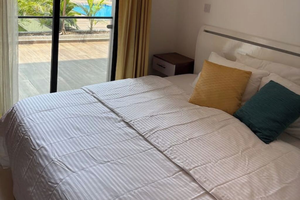 Une chambre d’hôtel avec un grand lit, une table de chevet et une vue sur la piscine, accessible par une porte coulissante.