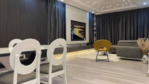 A modern living room with a dining area, featuring a sofa, a TV mounted on the wall, and a dining table with chairs.