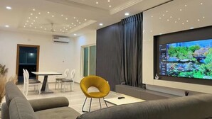 A modern living room with a flat-screen TV, a yellow chair, and a grey sofa.