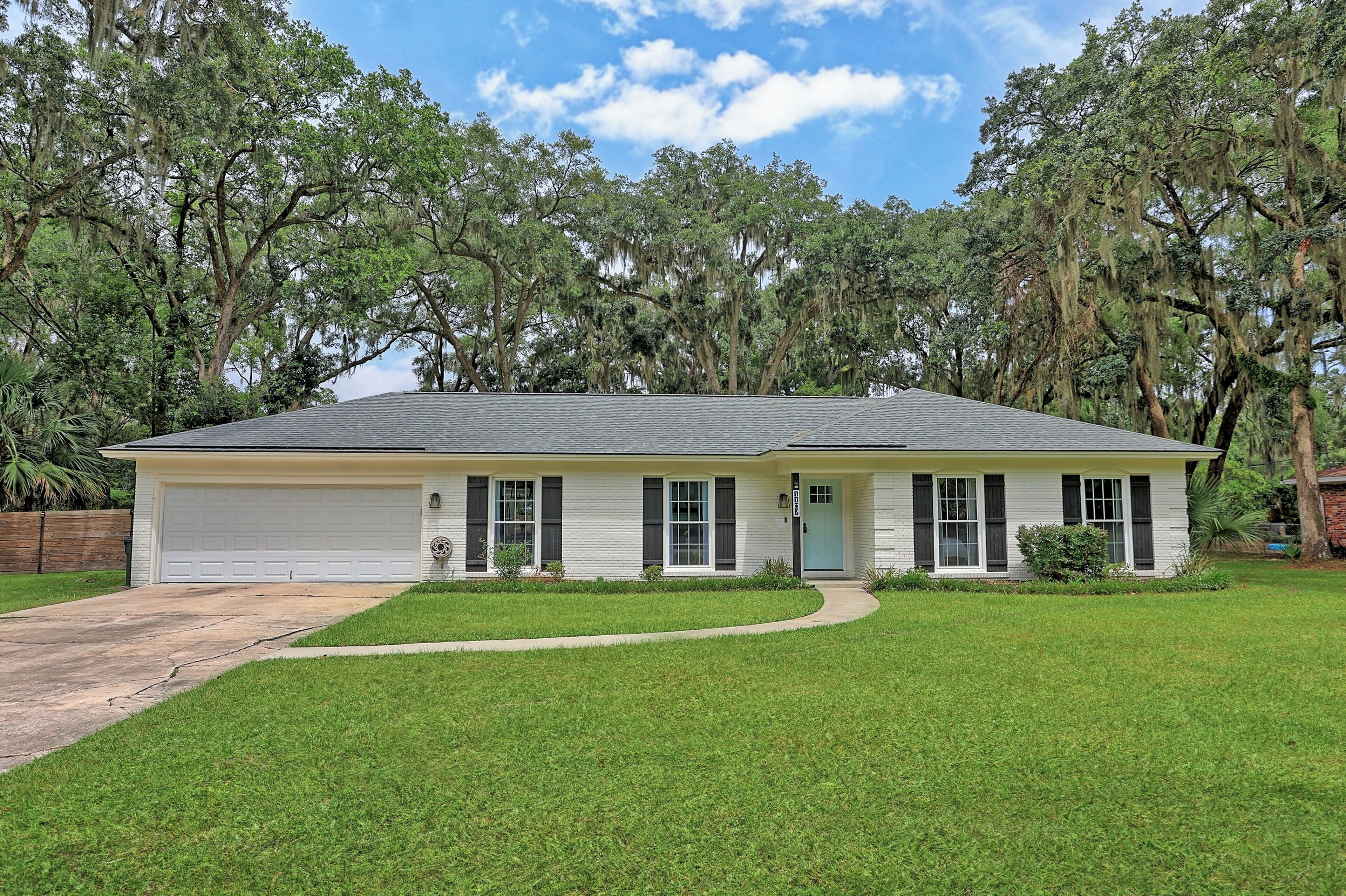 A single-story house with a garage, a front lawn, and mature trees in the background.