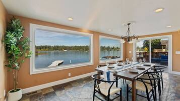 A dining area with a view of a lake, large windows, and a chandelier.