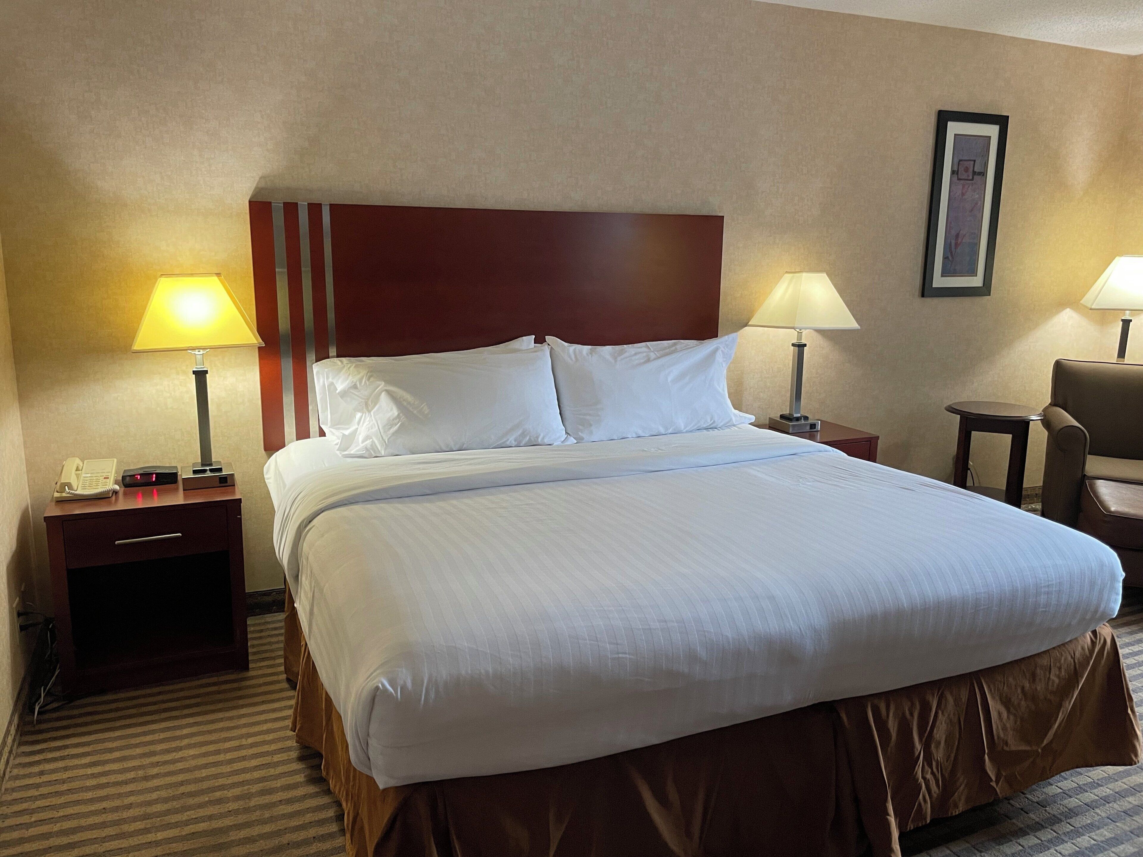 A hotel room with a large bed, two bedside tables with lamps, a chair, and a framed picture on the wall.