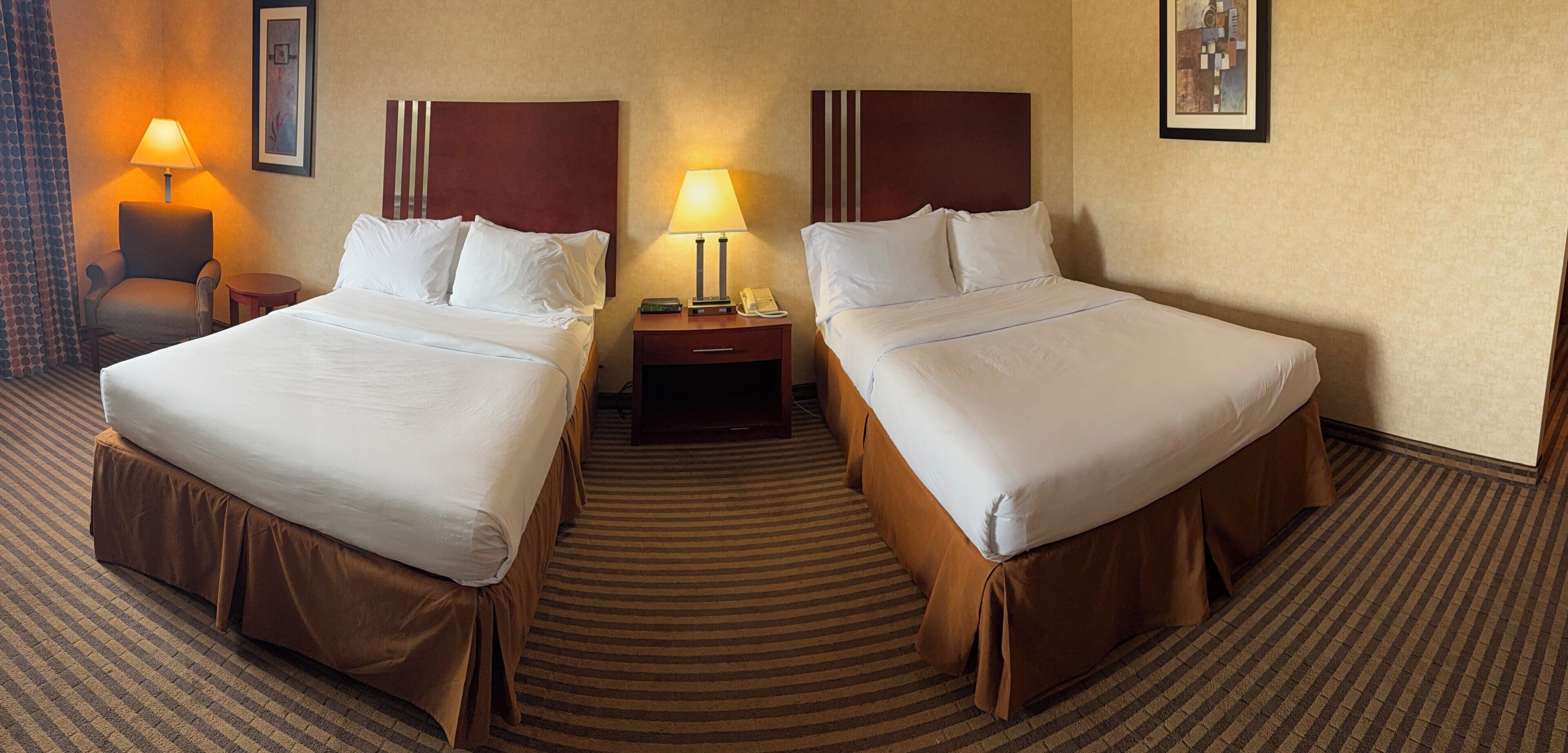 Een hotelkamer met twee bedden, een nachtkastje, een lamp, een stoel en een vloerbedekking.