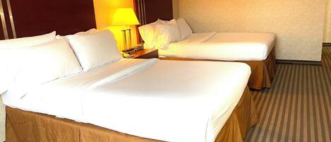 A hotel room with a large bed, two smaller beds, a nightstand with a lamp, and a framed picture on the wall.