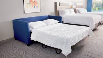 A hotel room with two beds, a blue sofa, and a large window.