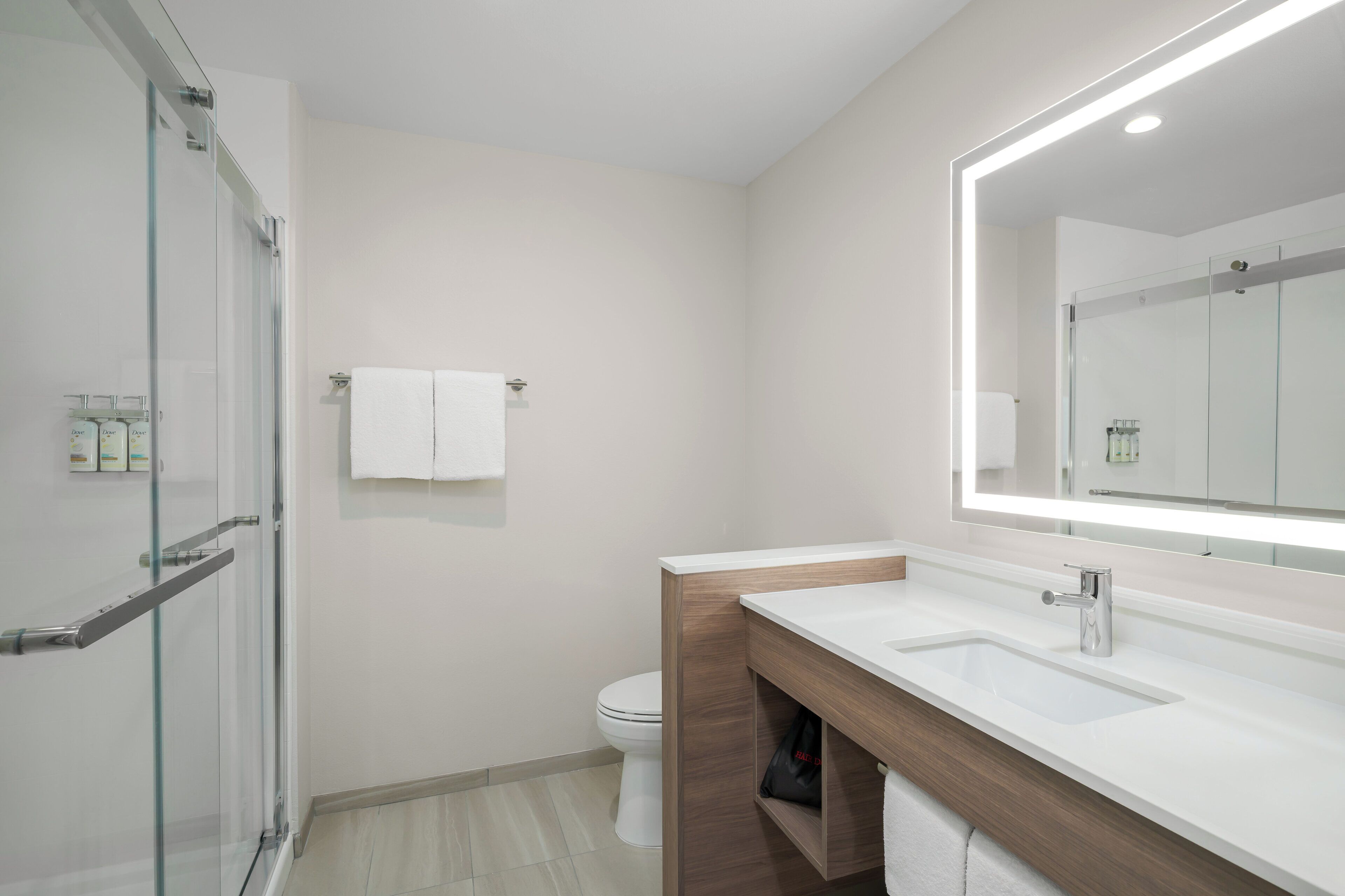 Un baño moderno con cabina de ducha de vidrio, inodoro blanco y tocador con espejo.