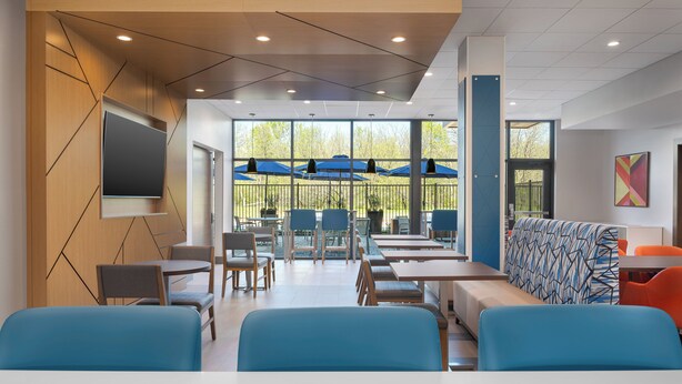 A modern dining area with tables and chairs, a large screen, and a view through large windows.