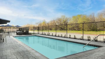 Una piscina rectangular con cerramiento de metal negro, solárium con baldosas y mobiliario exterior.