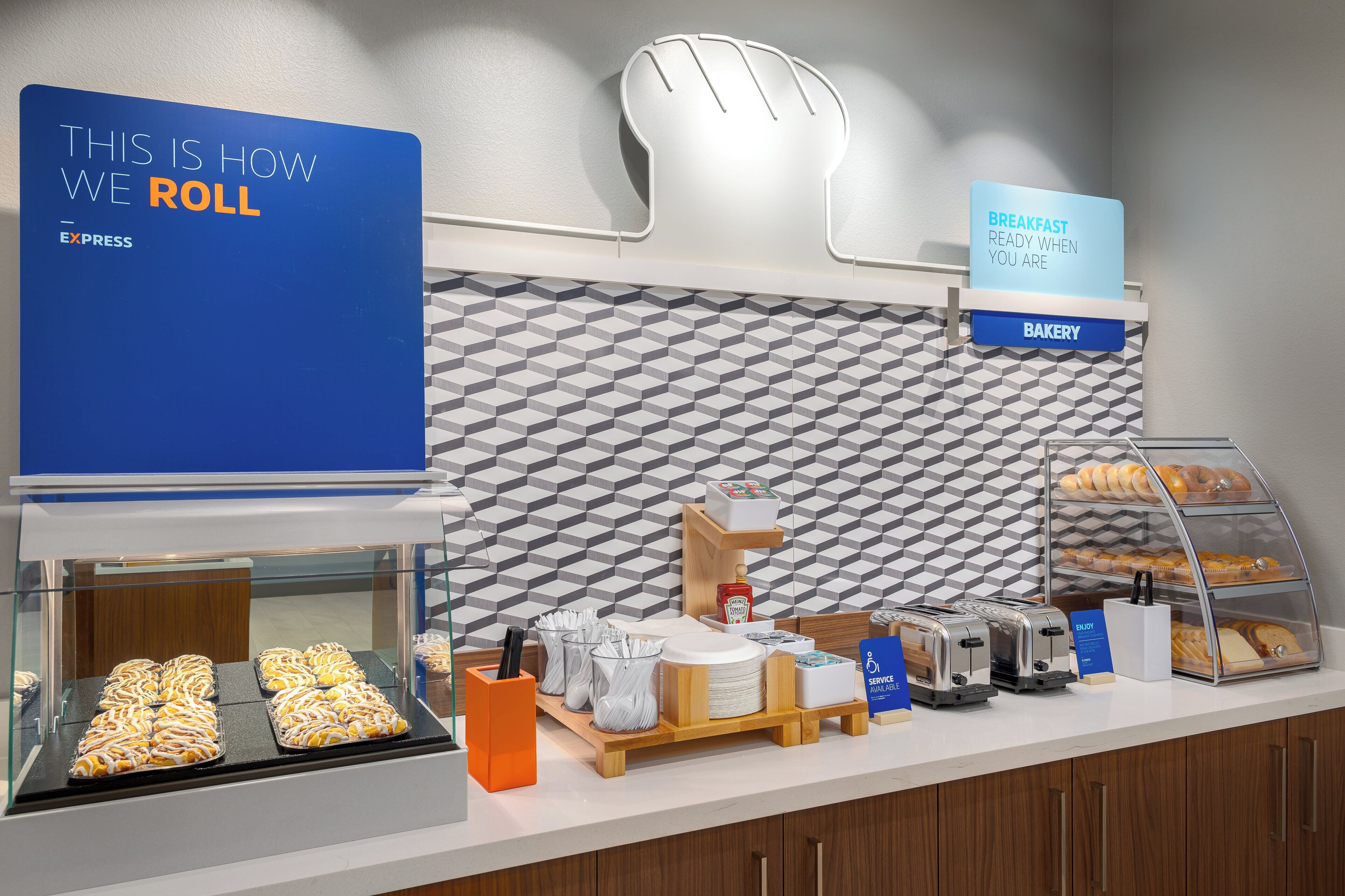 A breakfast buffet with a sign indicating 'Breakfast Ready When You Are' and a display of pastries and bread.