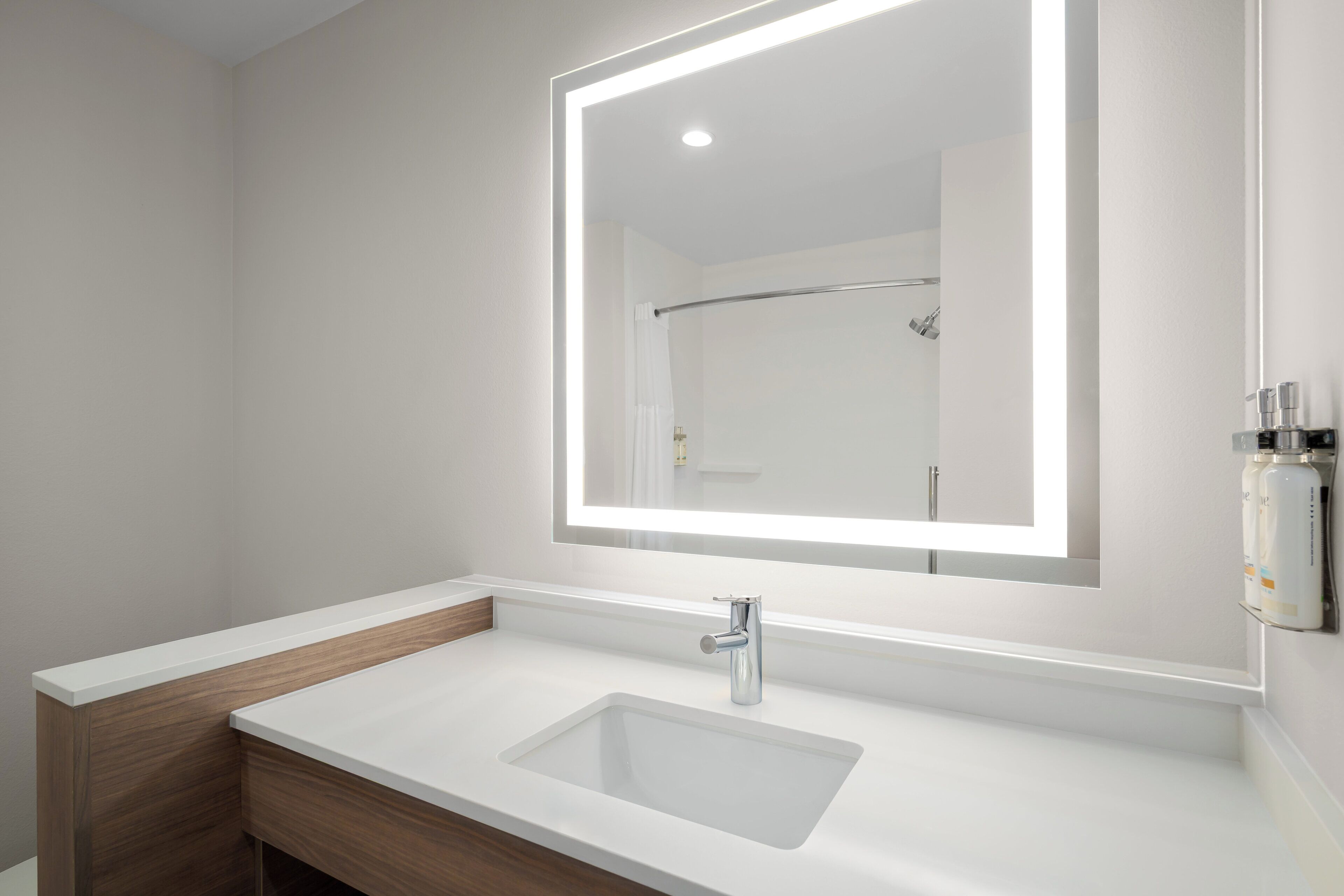 A modern bathroom with a white sink, a mirror, and a shower visible in the reflection.
