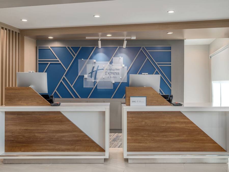 A reception desk with a blue and white geometric wall design, a wooden reception desk, and a sign indicating 'Holiday Inn Express & Suites.'