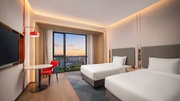 Habitación de hotel con dos camas, un escritorio, una silla, un televisor y un ventanal con vistas a la ciudad.