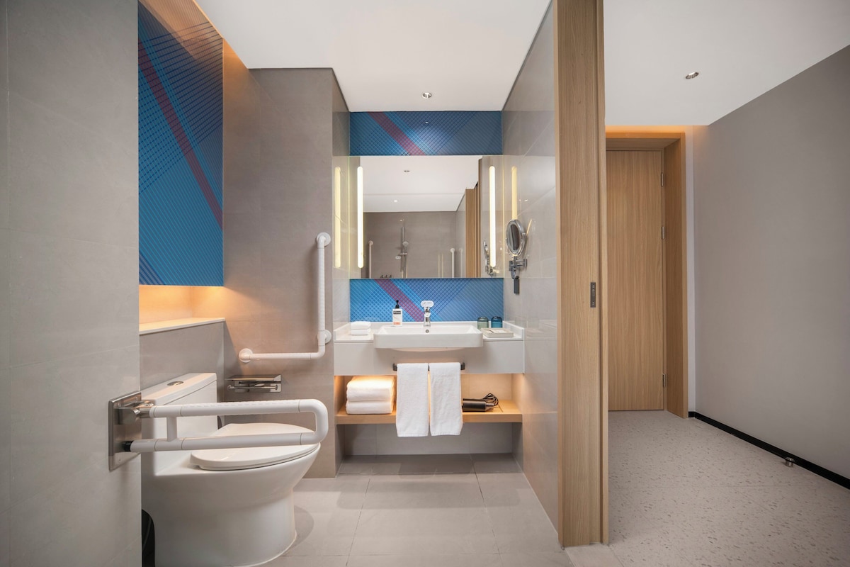 A modern bathroom with a toilet, sink, and mirror, featuring a towel rack and a shelf with toiletries.