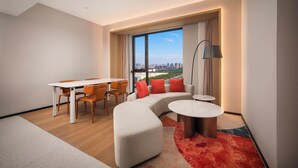 A modern living room with a dining area, a sofa, a round coffee table, and a large window with a city view. - Holiday Inn Express Beijing Tongzhou by IHG (Tongzhou)
