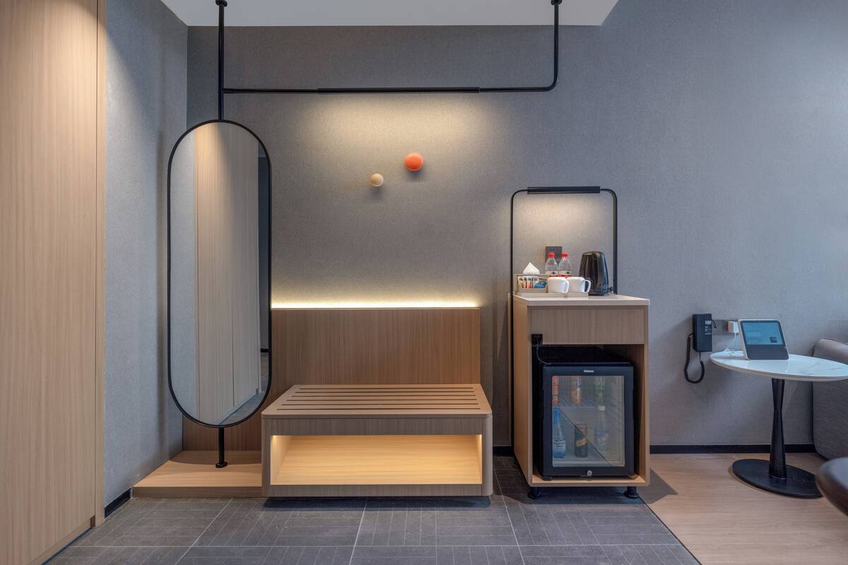 A modern, minimalist room with a wooden bench, a small refrigerator, a coffee machine, and a tablet on a table.