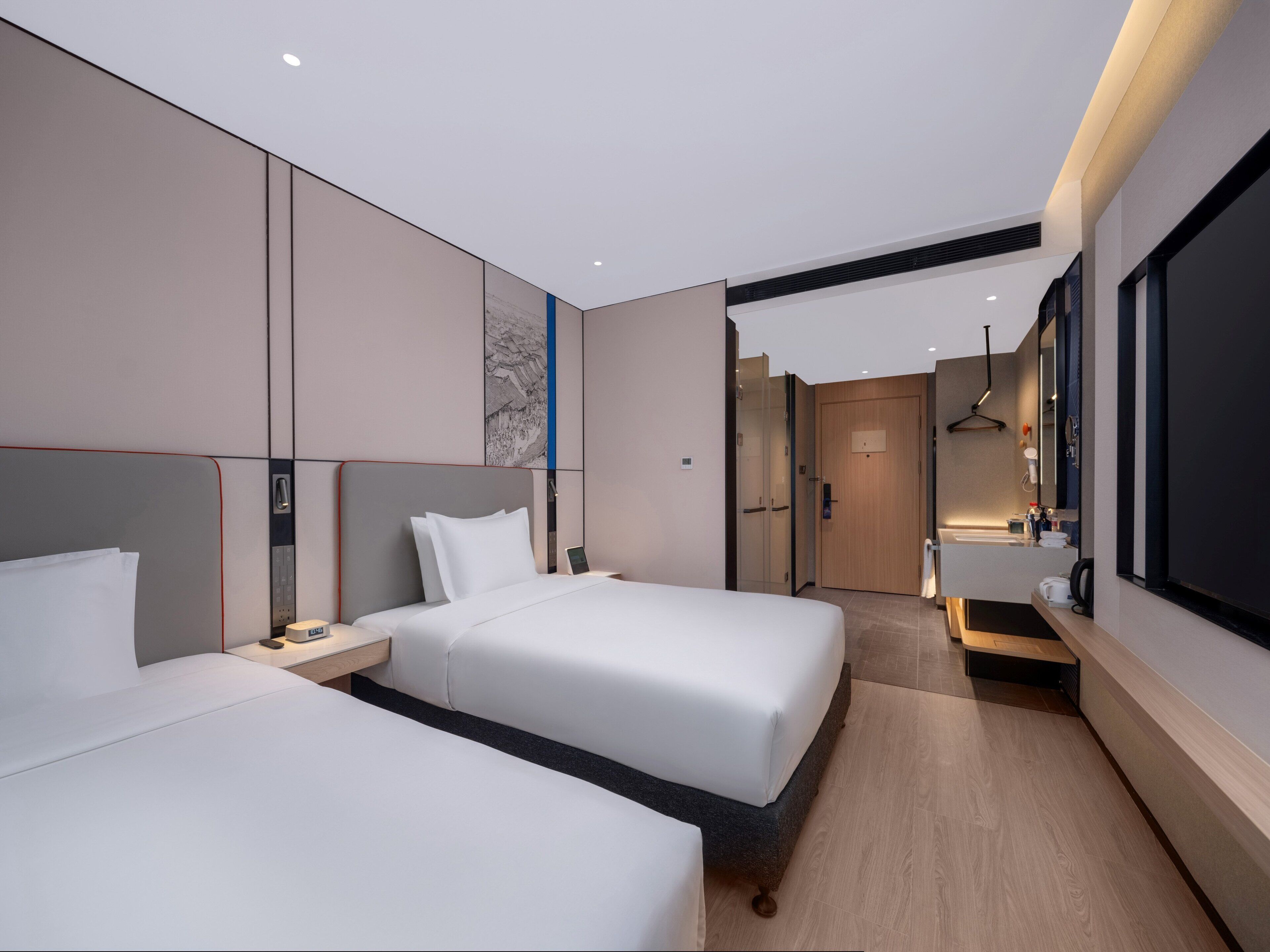 A modern hotel room with two beds, a large mirror, a wooden door, and a bathroom with a sink and mirror.
