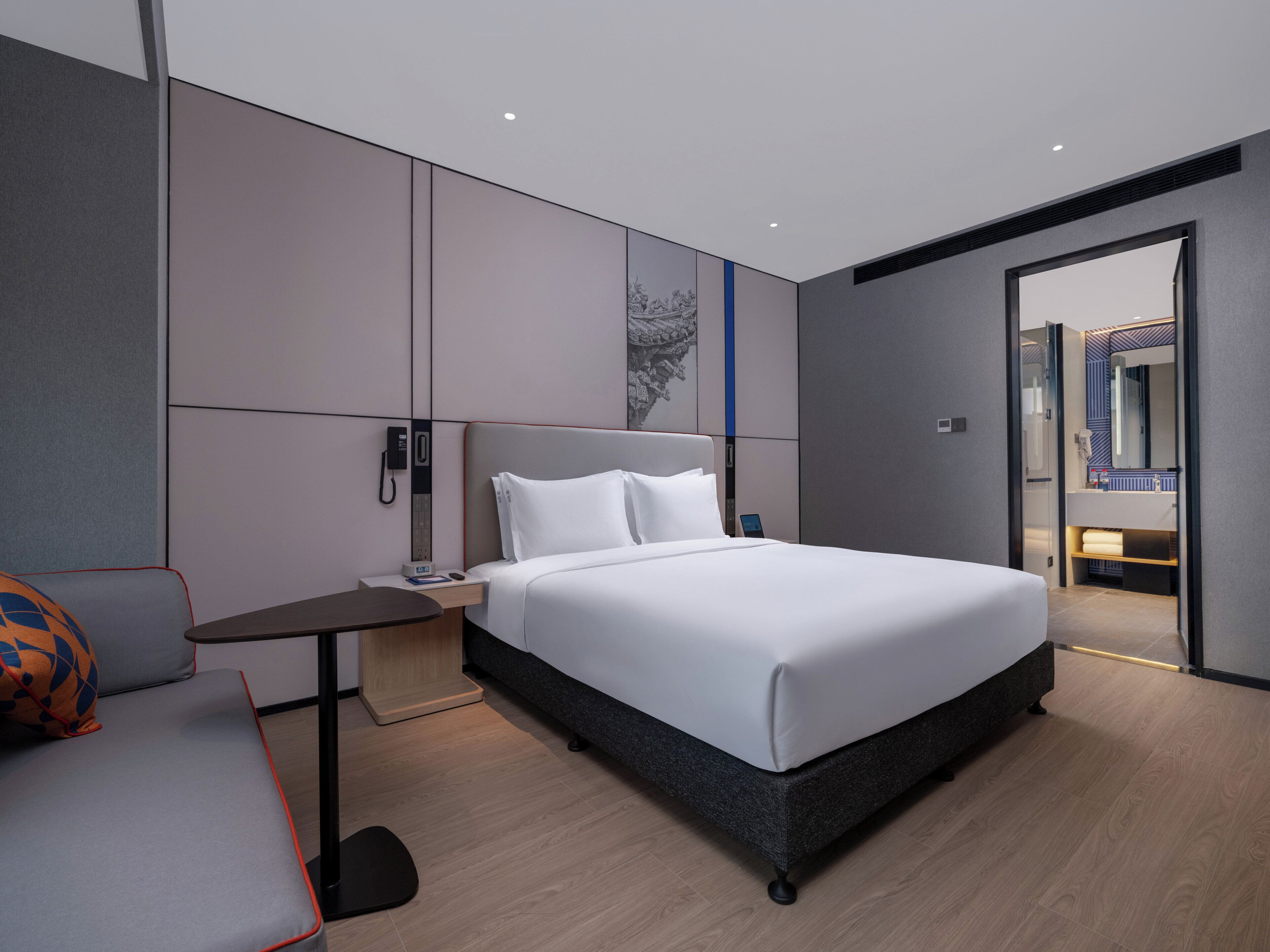 Een moderne hotelkamer met een groot bed, een nachtkastje met telefoon, een bureau met stoel, en een zichtbare badkamer door een geopende deur.