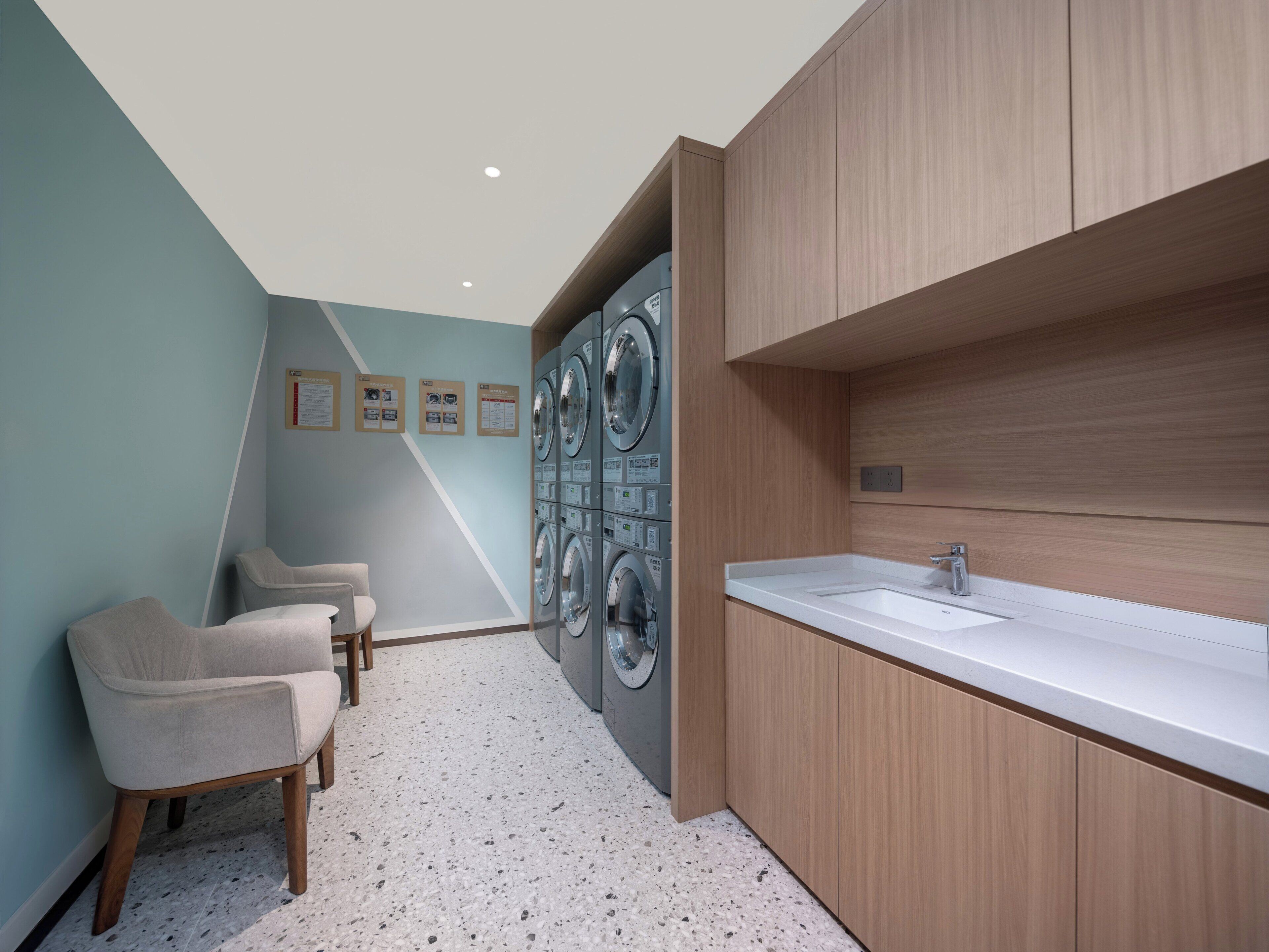 A modern bathroom with a sink, two chairs, and a wall-mounted washing machine.