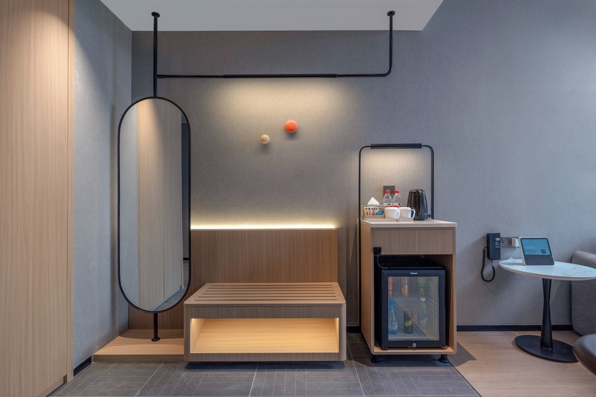 A modern, minimalist room with a wooden bench, a small refrigerator, a coffee machine, and a tablet on a table.