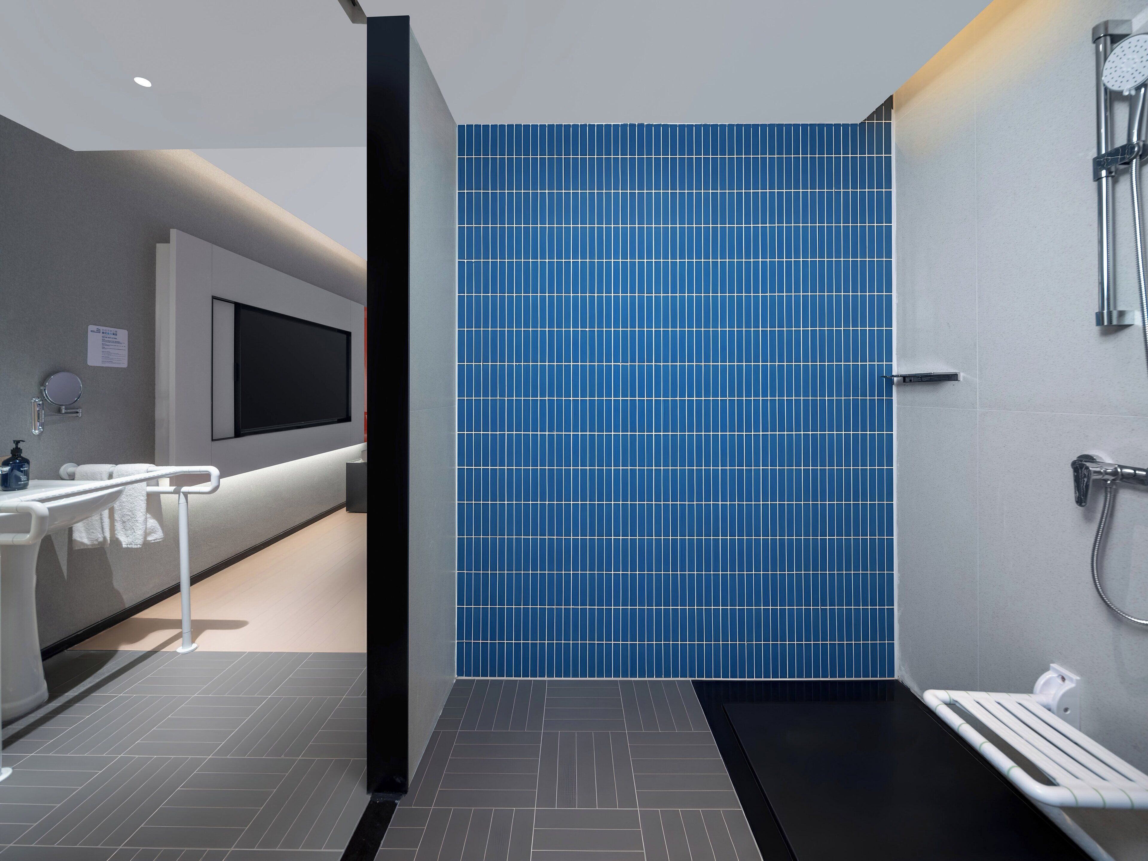 A modern bathroom with a large mirror, a sink, and a shower area with a blue-tiled wall.