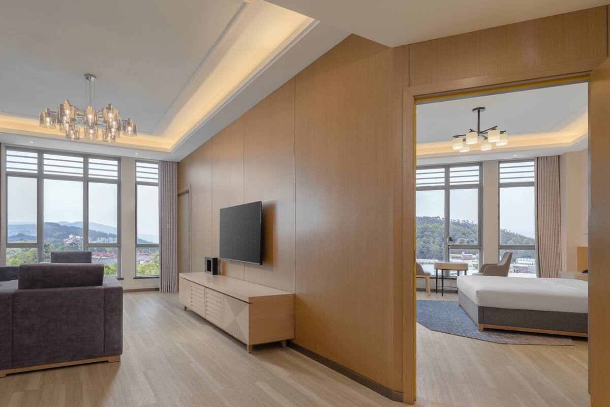 A modern hotel room with a sofa, a TV, a wooden cabinet, and a bed.