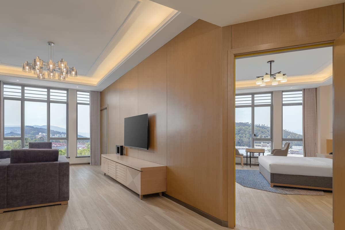 A modern hotel room with a sofa, a TV, a wooden cabinet, and a bed.