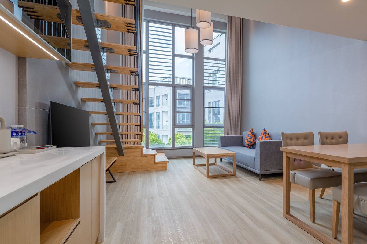 A modern living space with a staircase, a sofa, a dining table, and a TV.