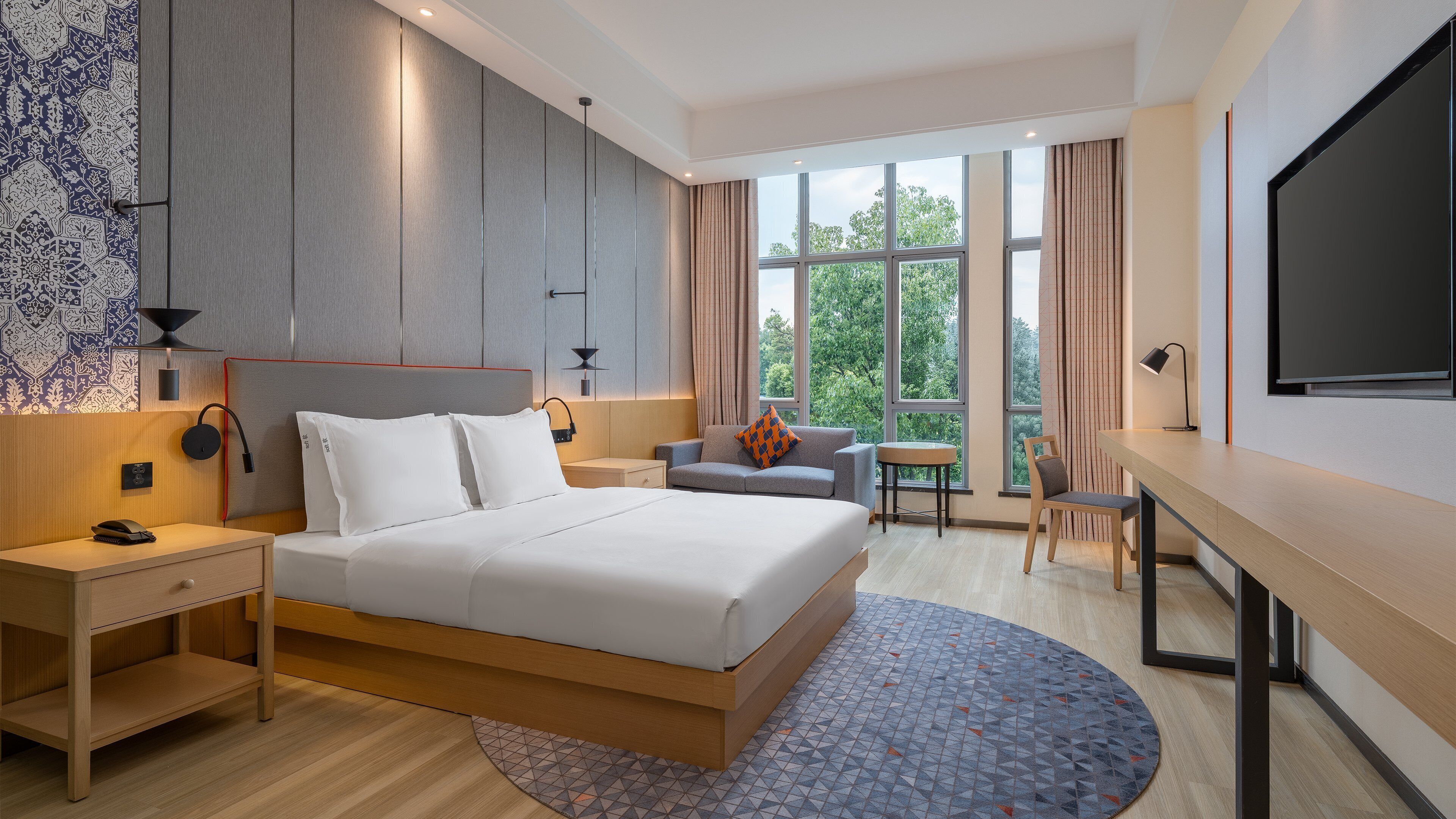 A modern hotel room with a large bed, a desk, a chair, and a TV.