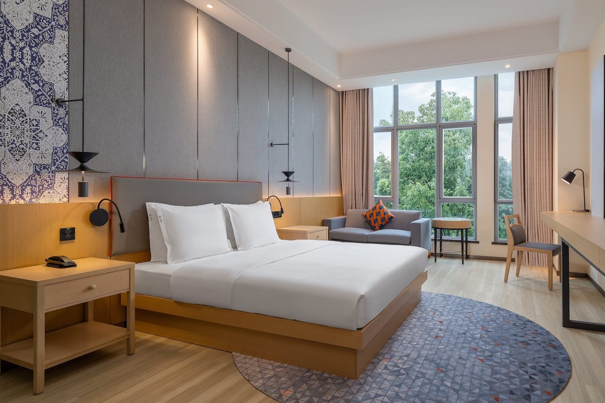 A modern hotel room with a large bed, a desk, a chair, and a TV.