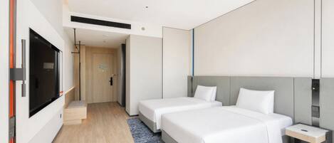A modern hotel room with two beds, a TV, and a small desk.