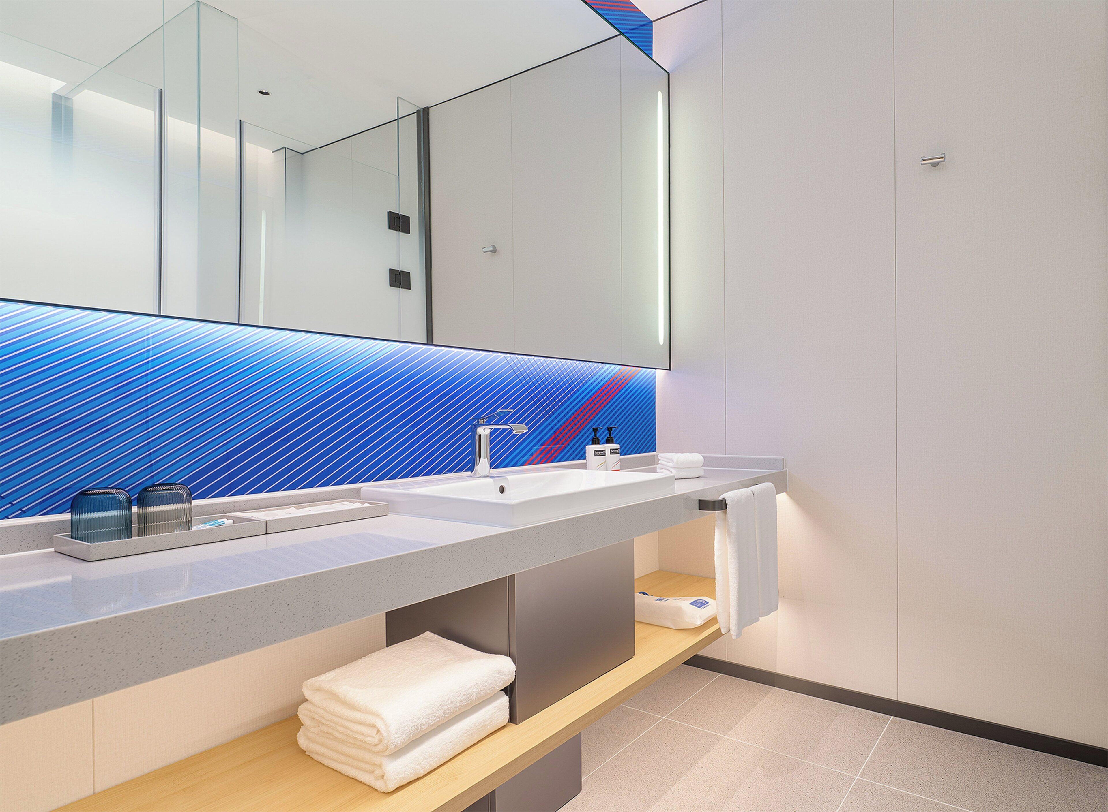 A modern bathroom with a large mirror, two sinks, and a blue patterned wall.