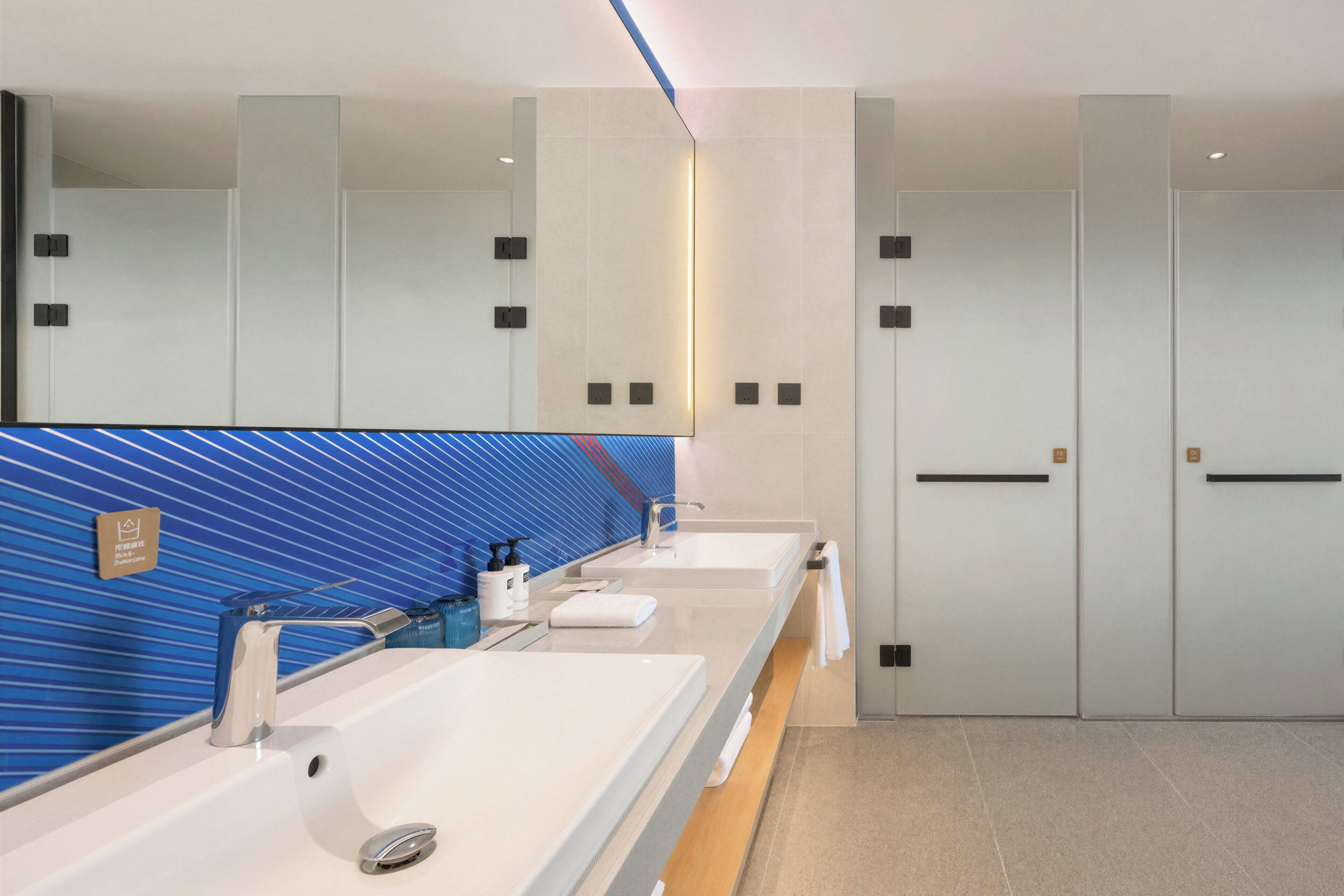 A modern bathroom with two sinks, a mirror, and a blue tiled wall.